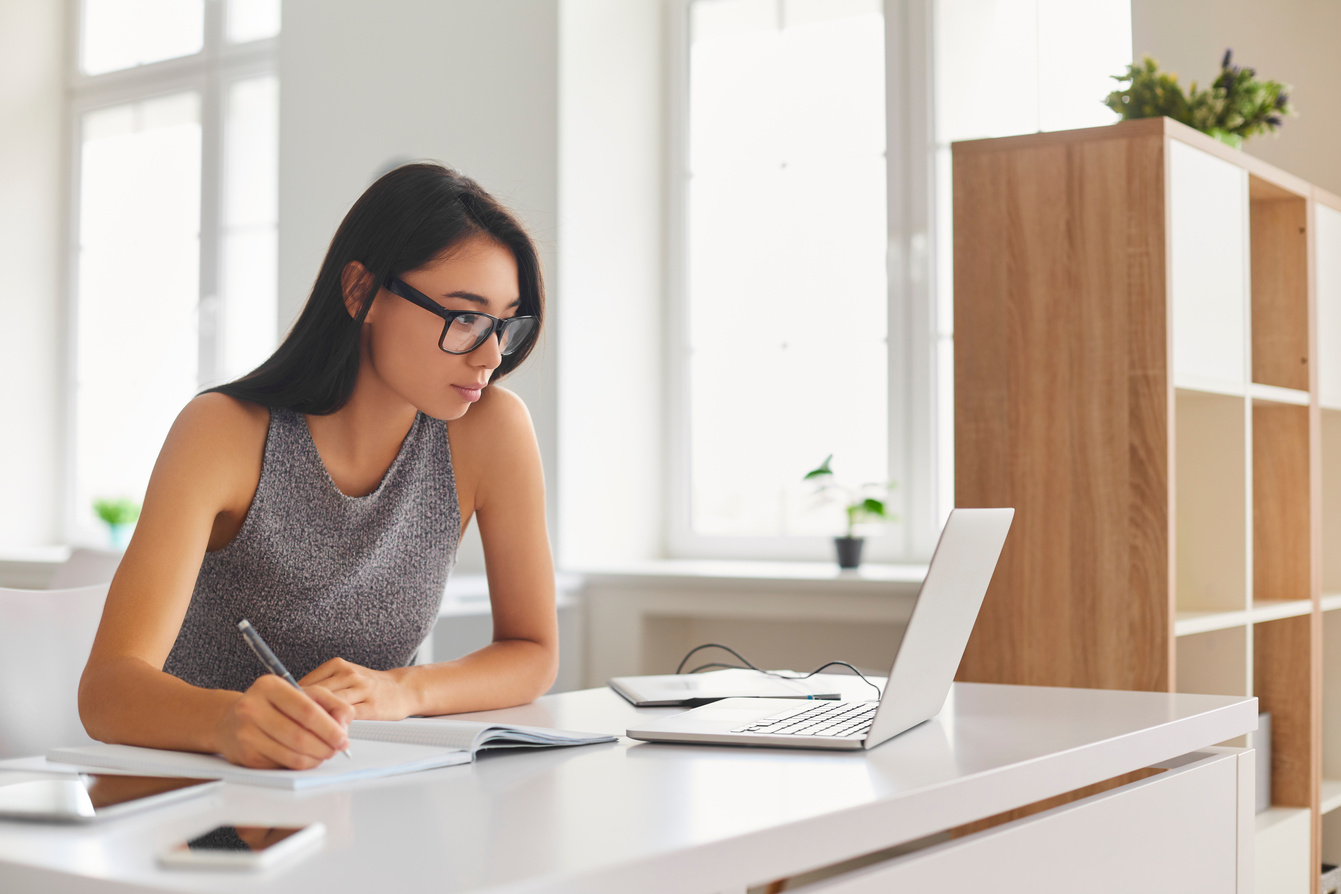 Bright Student Taking Notes in Notebook and Using Laptop Computer for E-Learning