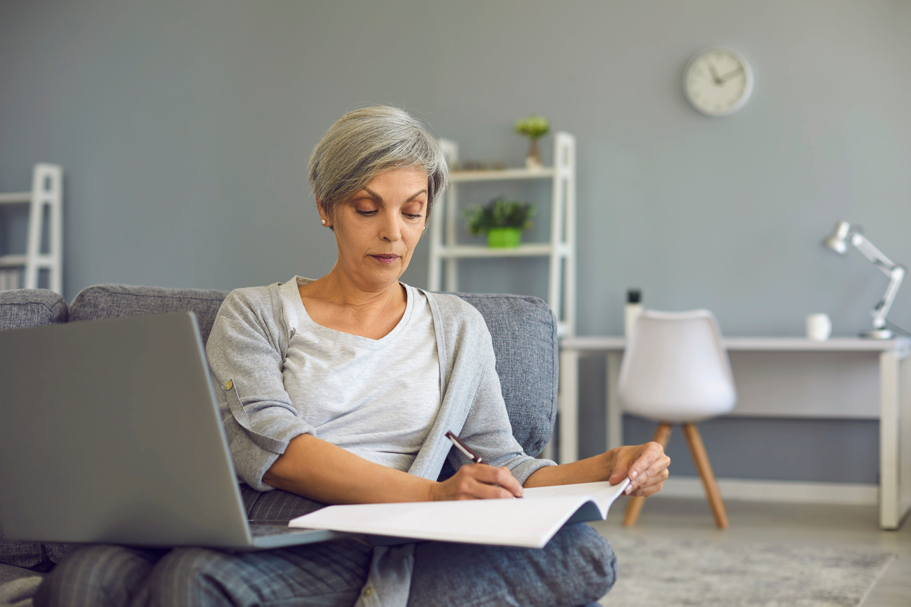 Senior Woman Making Notes during Online Lesson on Laptop at Home