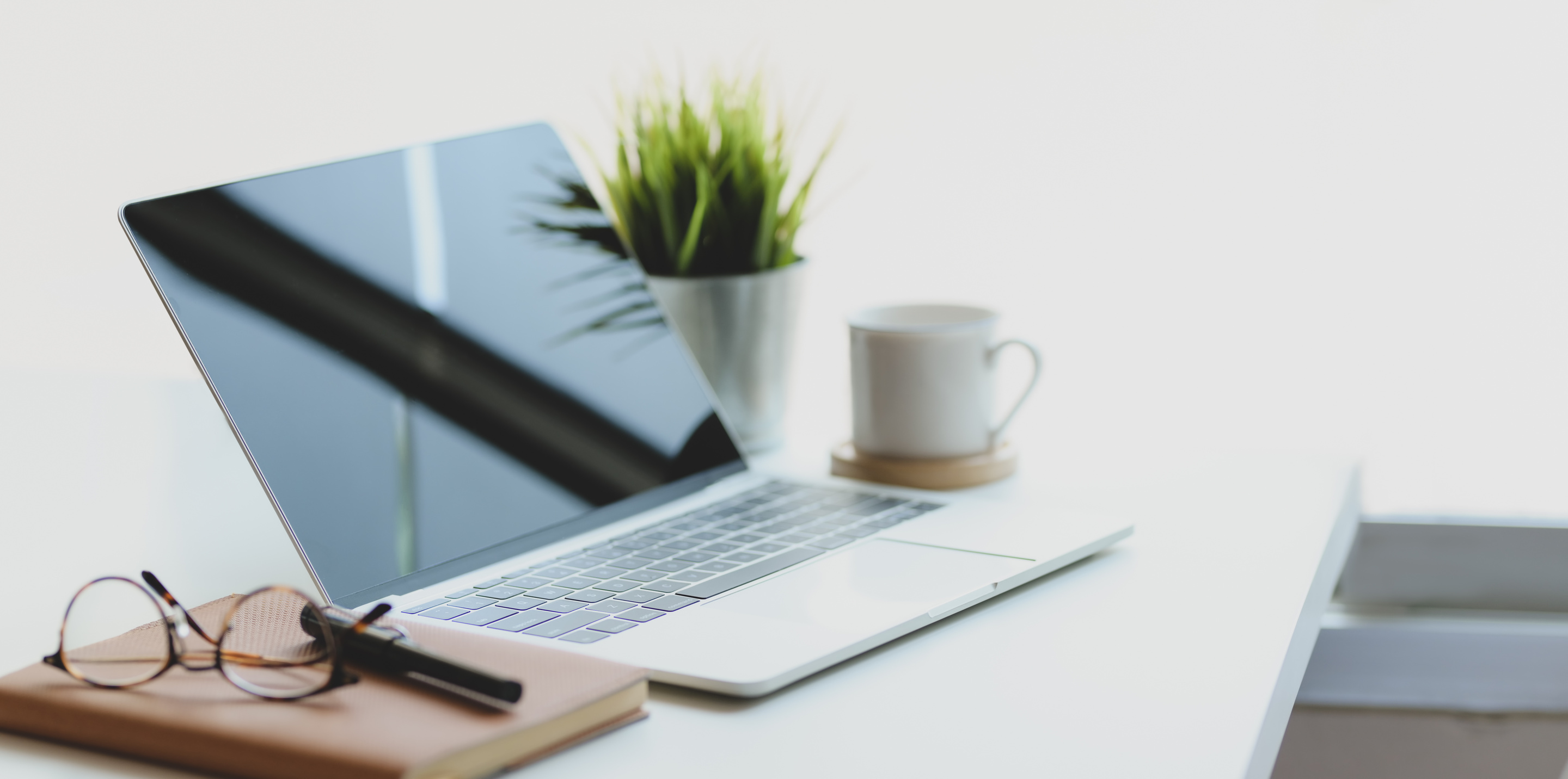 Laptop placed on desk with notebook and mug